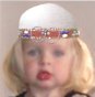 Kopfschmuck eines etwa dreijährigen Mädchens. Verschiedene Perlen wurden in Dreiergruppen auf einem Stoffband aufgenäht, wobei nur die hinteren Enden des Stoffs freiblieben. Das Zentrum schmückten zwei S-Schleifenringe, auf die je eine kleine Perle aufgeschoben war.