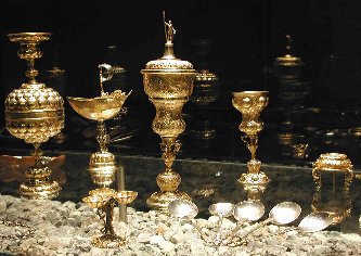 Neben Pokalen ist das teilvergoldete Fortunaschiffchen zu sehen, davor ein Salzfass mir drei Schalen. Rechts im Vordergrund silberne Löffel.