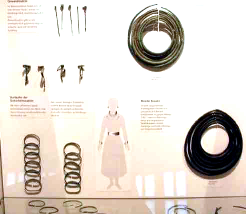 Oben eine Reihe von Gewandnadeln,  Fibeln als Gewand- schlieen und darunter Stze von Armringen. Die Halsringe wurden hnlich wie bei den Frauen der Massai als Hals- kragen getragen.